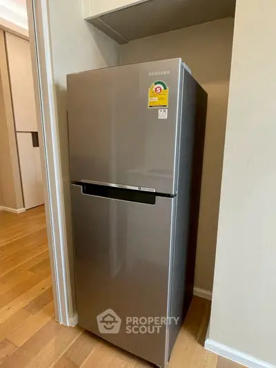 Modern stainless steel refrigerator in a sleek kitchen setting with wooden flooring.