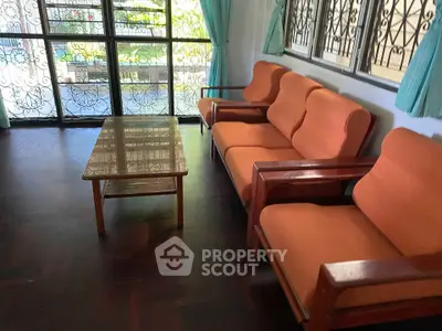 Spacious living room with vintage orange sofas and large windows offering garden views.