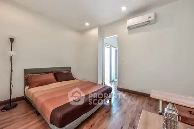Modern bedroom with wooden flooring and air conditioning, featuring stylish decor and natural lighting.