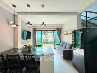 Modern living room with open layout and stylish lighting, featuring a cozy sofa and large windows overlooking a garden.