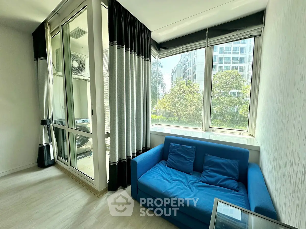 Bright living room with large windows and blue sofa, offering a view of lush greenery outside.