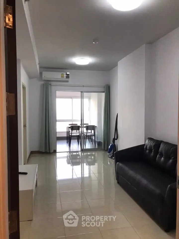 Spacious living room with modern sofa and dining area, featuring sleek tile flooring and natural light.
