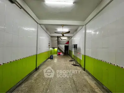 Spacious hallway with vibrant green and white tiles, featuring a ceiling fan and staircase.