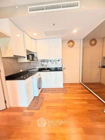 Modern kitchen with sleek cabinets, washing machine, and wooden flooring in a stylish apartment.