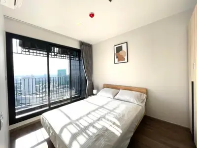 Bright bedroom with large window and city view, featuring a cozy bed and modern decor.