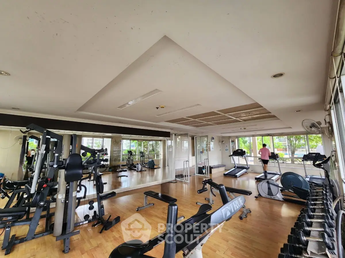 Spacious gym with modern equipment and large windows offering natural light.