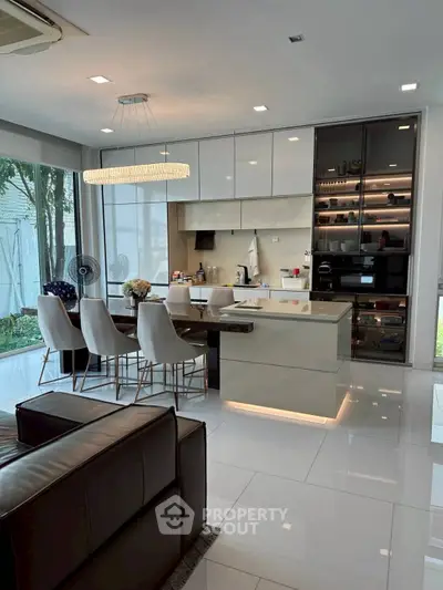 Modern open-layout kitchen with sleek design and dining area, featuring elegant lighting and large windows.