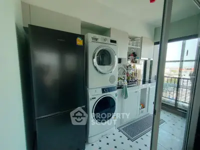 Modern laundry area with stacked washer dryer and sleek black fridge in bright space.