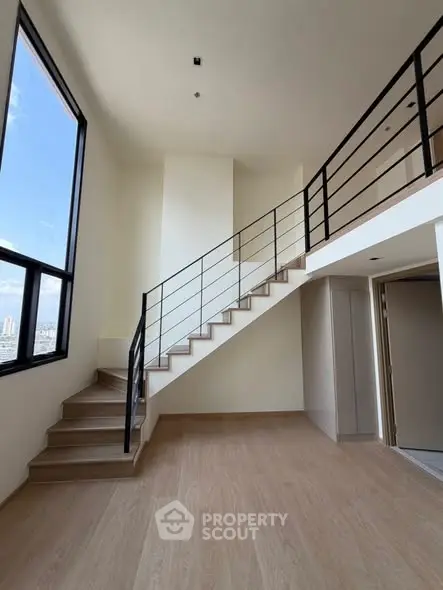 Spacious modern duplex with large windows and sleek staircase, offering abundant natural light and city views.