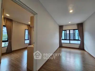 Spacious empty room with wooden flooring and large windows in modern apartment.