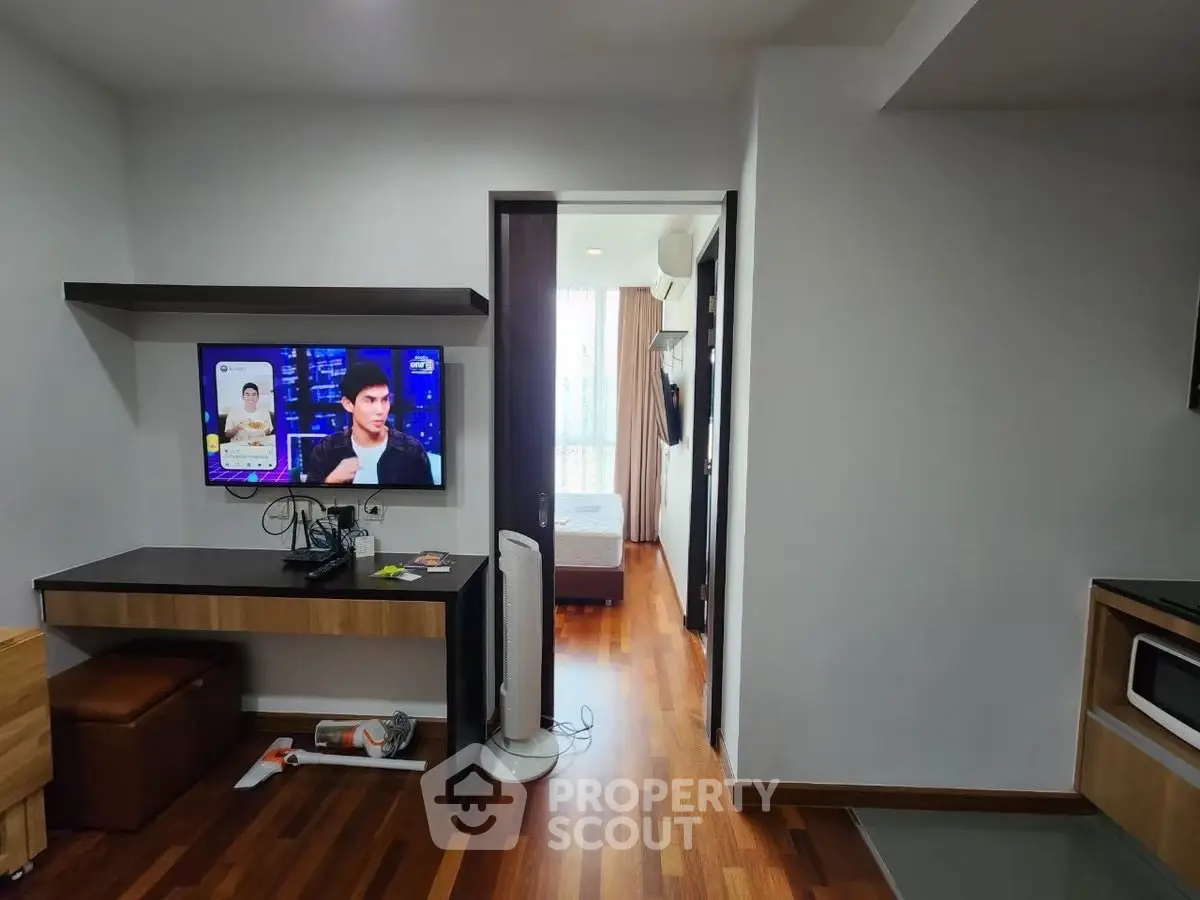 Modern apartment interior with wooden flooring, TV, and view into bedroom