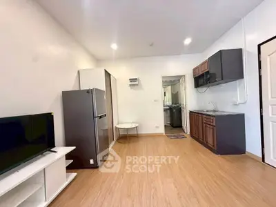 Modern open-plan living room with kitchen, featuring sleek appliances and wooden flooring.