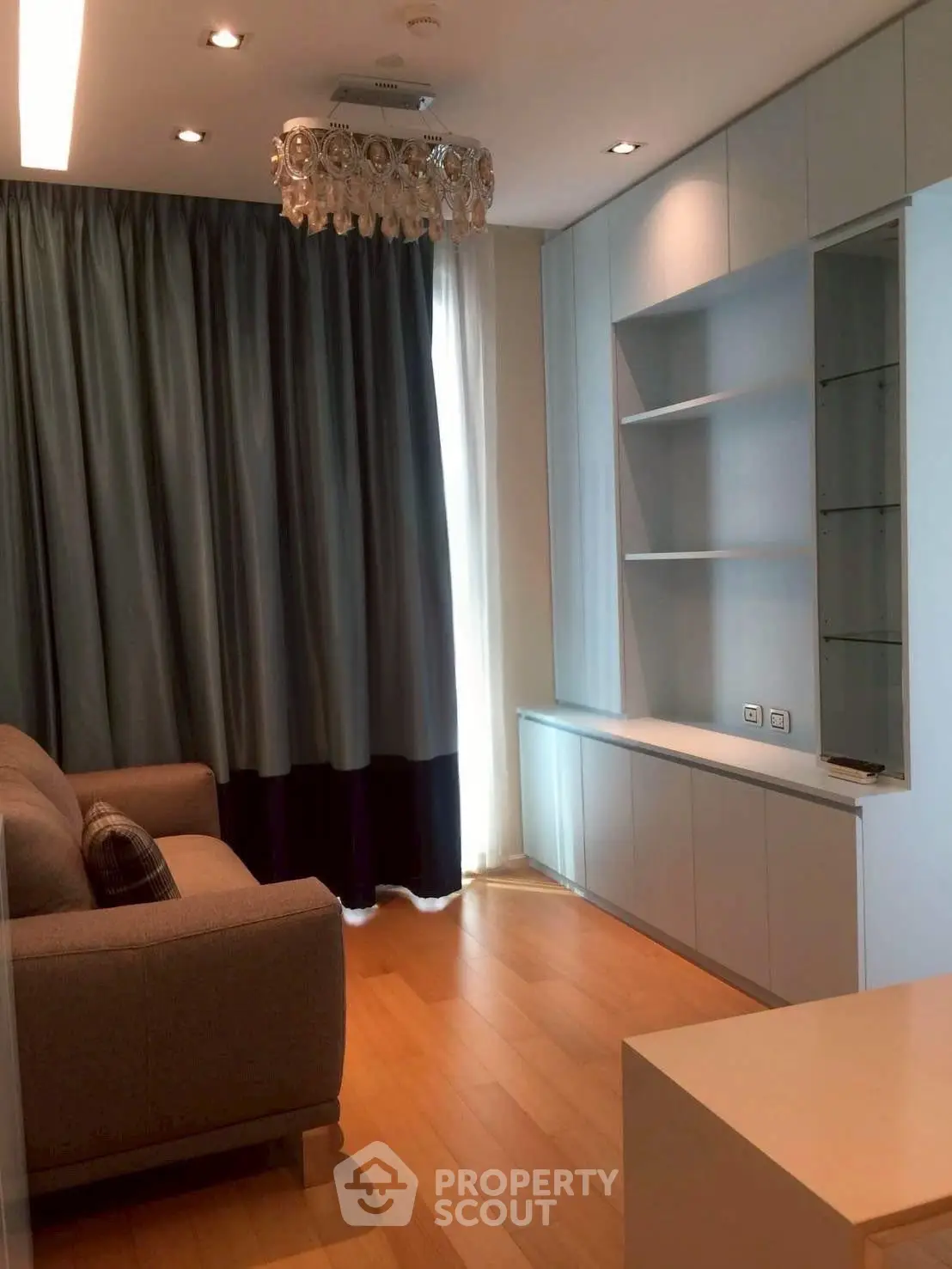 Modern living room with elegant chandelier and built-in shelving, featuring cozy sofa and floor-to-ceiling curtains.