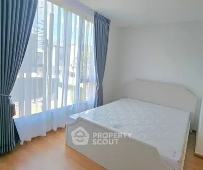 Bright bedroom with large windows and elegant curtains, featuring a comfortable bed and wooden flooring.