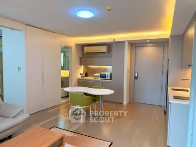 Modern open-plan living room with dining area and kitchenette, featuring sleek design and warm lighting.