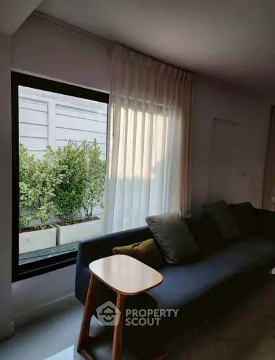 Cozy living room with large window and modern sofa, offering a serene view of greenery.