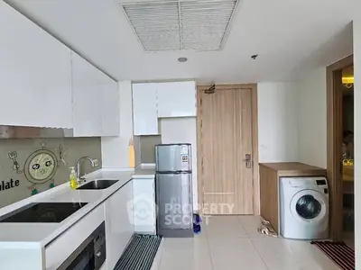 Modern kitchen with sleek white cabinets and appliances including washing machine and oven.