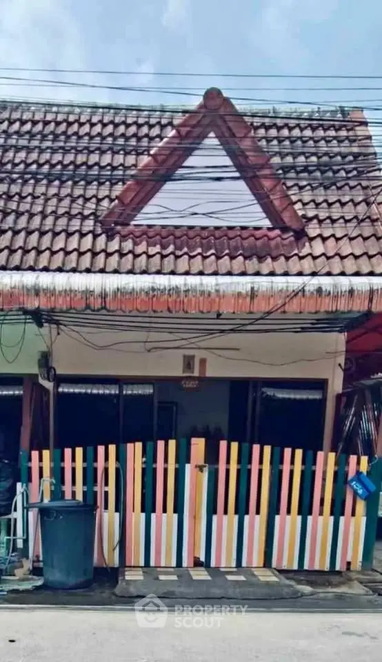 Charming small house with colorful fence and unique triangular roof design.