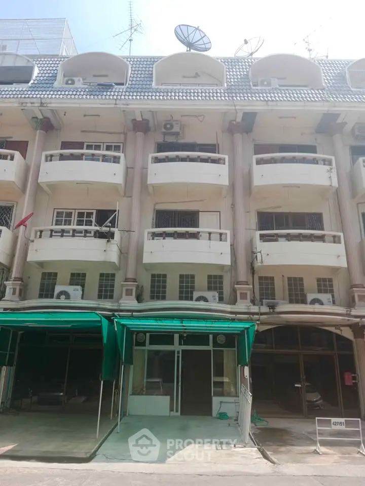Charming multi-story building with balconies and green awnings, perfect for urban living.