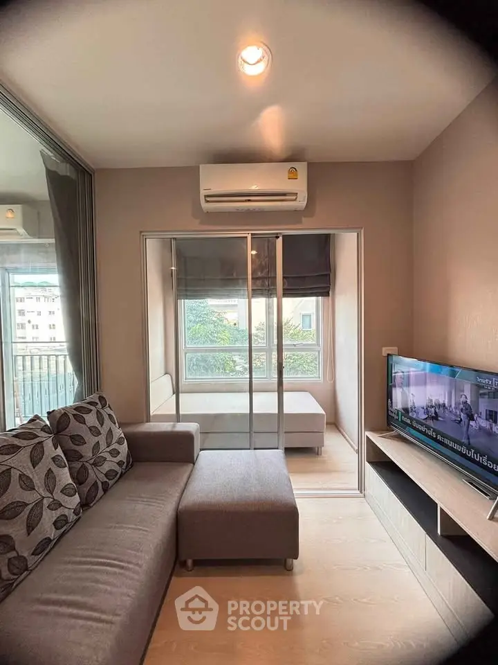 Cozy living room with modern sofa and TV, featuring a view of the city through large windows.