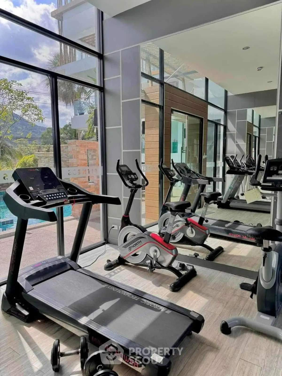 Modern gym with cardio equipment and pool view in luxury real estate property.