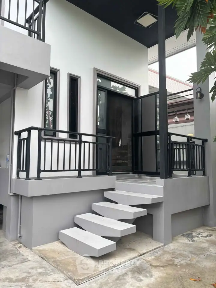 Modern exterior entrance with sleek black railings and concrete steps leading to a stylish glass door.
