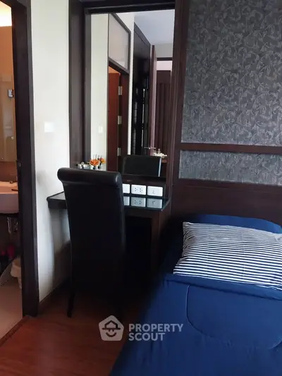 Cozy bedroom with modern decor and adjacent bathroom, featuring a sleek desk and comfortable bed.
