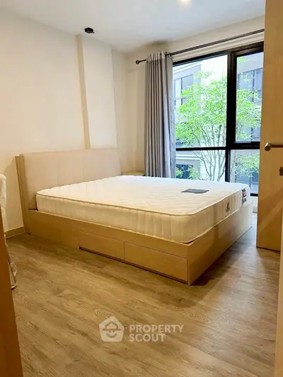 Cozy bedroom with large window and wooden flooring in modern apartment.