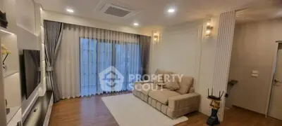 Elegant living room with cozy beige sofa and modern lighting, featuring large windows and stylish curtains.