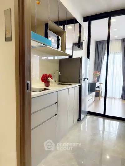 Modern kitchen with sleek cabinetry and open layout leading to a bright living area with large windows.