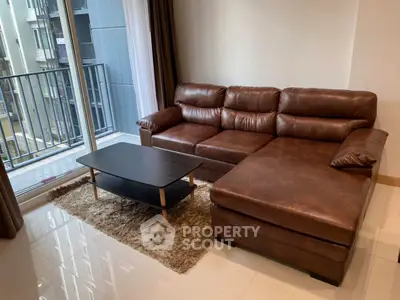 Modern living room with brown leather sofa and balcony view in urban apartment.