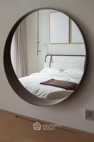 Elegant bedroom with modern decor reflected in a round mirror, featuring a cozy bed and minimalist design.