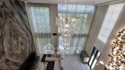 Luxurious living room with high ceilings, elegant chandelier, and floor-to-ceiling windows.