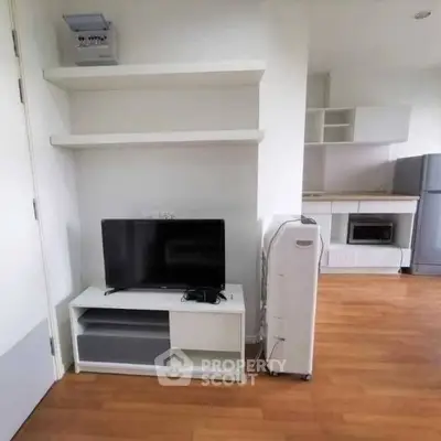 Modern apartment interior with TV, shelves, and kitchen appliances.