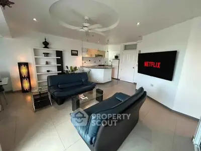 Modern living room with sleek furniture and open kitchen layout, featuring a large TV and stylish decor.