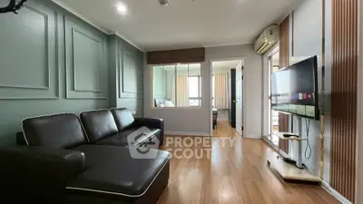 Modern living room with sleek black sofa and wall-mounted TV, featuring elegant wood flooring and stylish decor.