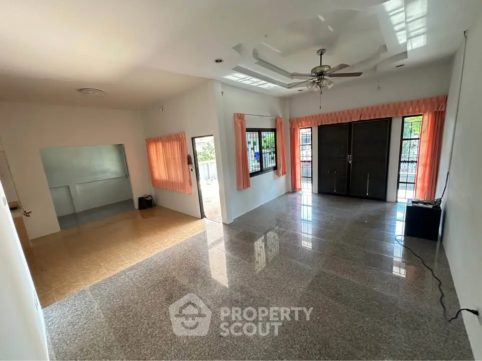 Spacious living room with large windows and ceiling fan, featuring glossy tiled floors and peach curtains.
