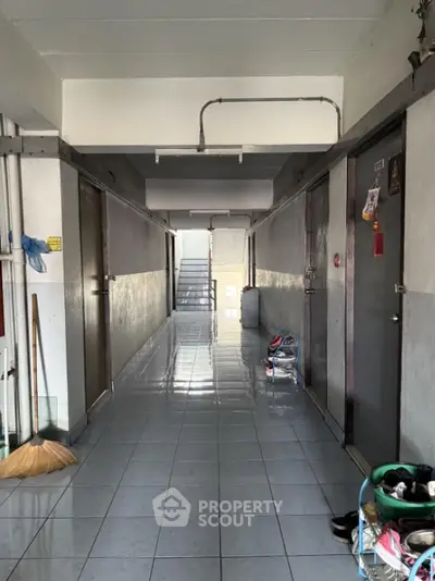 Apartment corridor with tiled floor and utility items, showcasing a typical residential hallway.