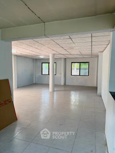 Spacious open-plan room with tiled flooring and natural light, ideal for versatile living or office space.