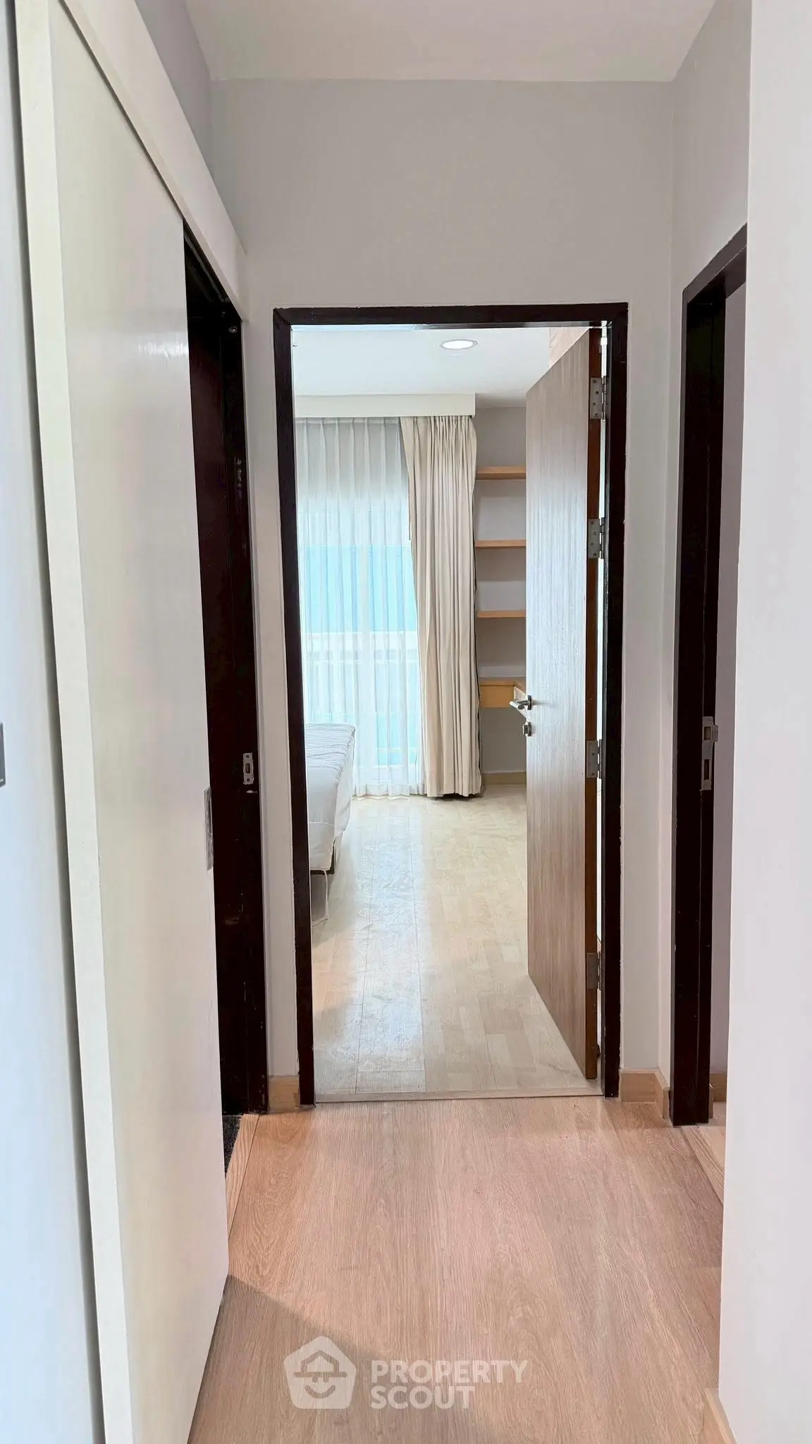 Bright hallway leading to a cozy bedroom with wooden flooring and natural light.