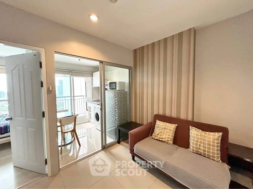 Modern living room with sofa, open kitchen, and balcony view in urban apartment.