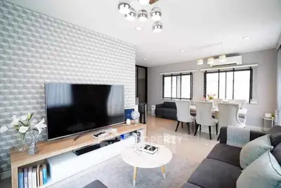 Modern living room with stylish decor and large TV, open dining area, and elegant lighting.