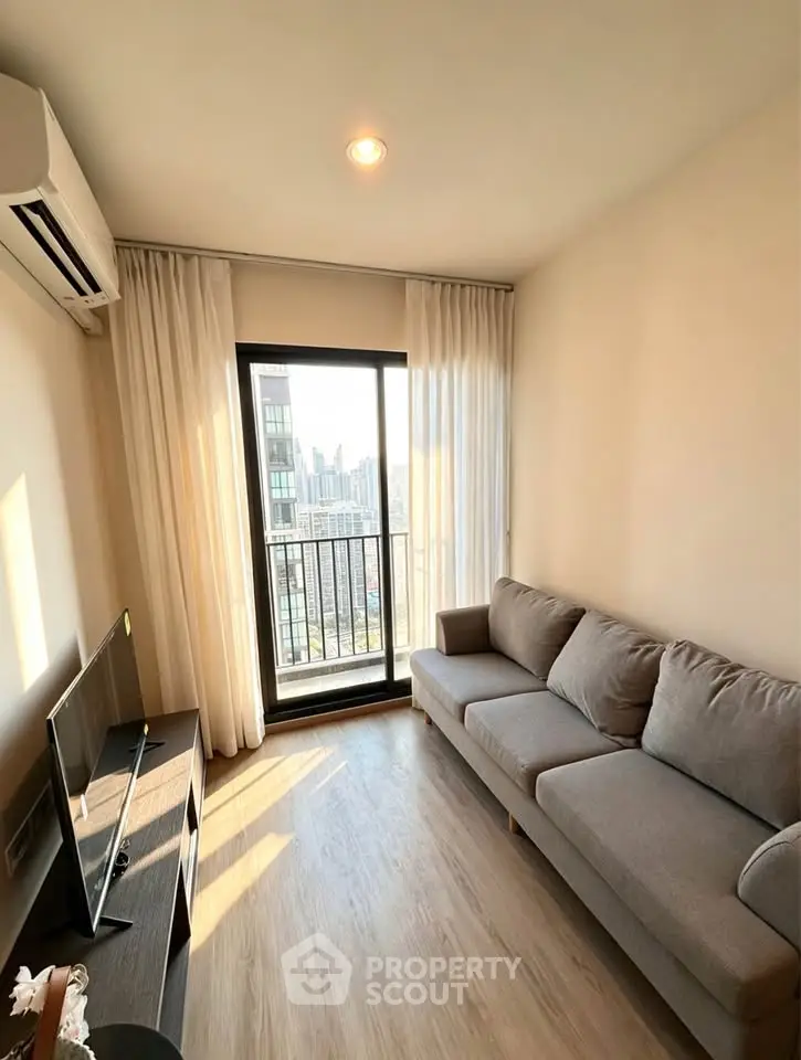 Modern living room with balcony view in a high-rise apartment, featuring sleek furniture and natural light.