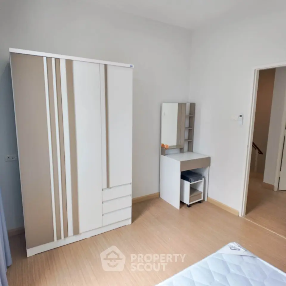 Minimalist bedroom with sleek wardrobe and compact vanity set, featuring light wood flooring and neutral walls.