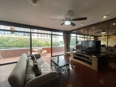 Spacious living room with large windows and balcony access, featuring modern furniture and ceiling fan.