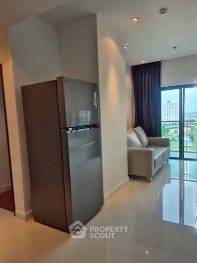 Modern apartment interior with sleek fridge and cozy living area featuring a sofa and city view.