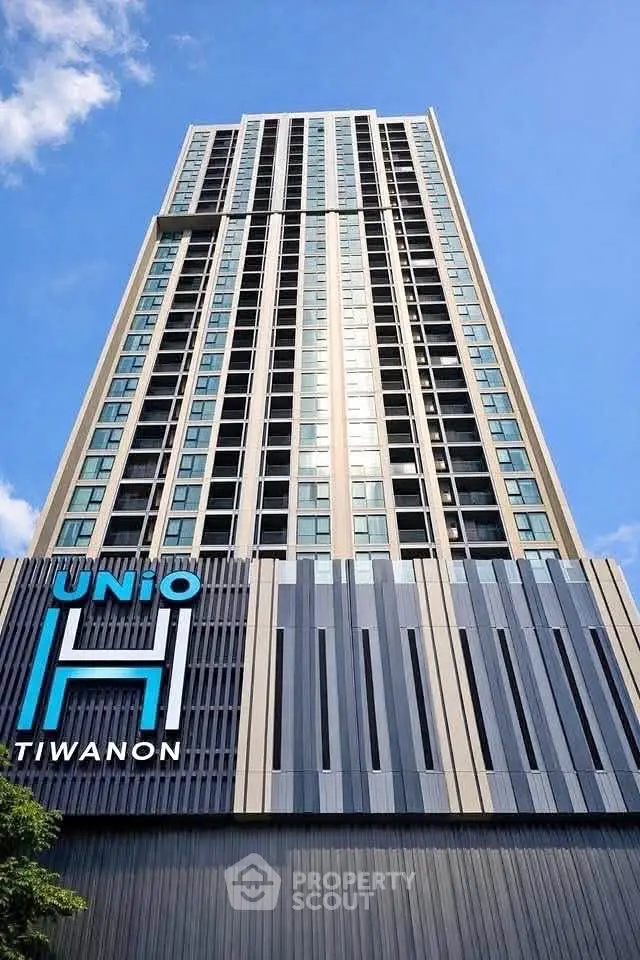 Modern high-rise building with sleek facade and blue sky backdrop, showcasing urban living at Unio Tiwanon.