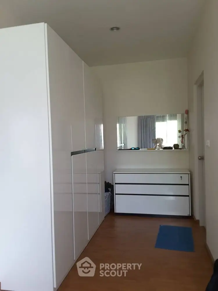 Modern bedroom with sleek white wardrobe and dresser, featuring a large mirror.