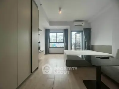 Modern minimalist bedroom with large window and city view, featuring sleek furniture and ample natural light.