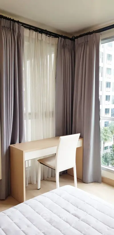 Bright bedroom with modern desk and chair, large windows with curtains, and a cozy bed.